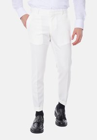 Pantaloni bianchi su misura con una finitura liscia, caratterizzati da una parte anteriore piatta, due tasche laterali e gambe con pieghe, abbinati a scarpe nere.