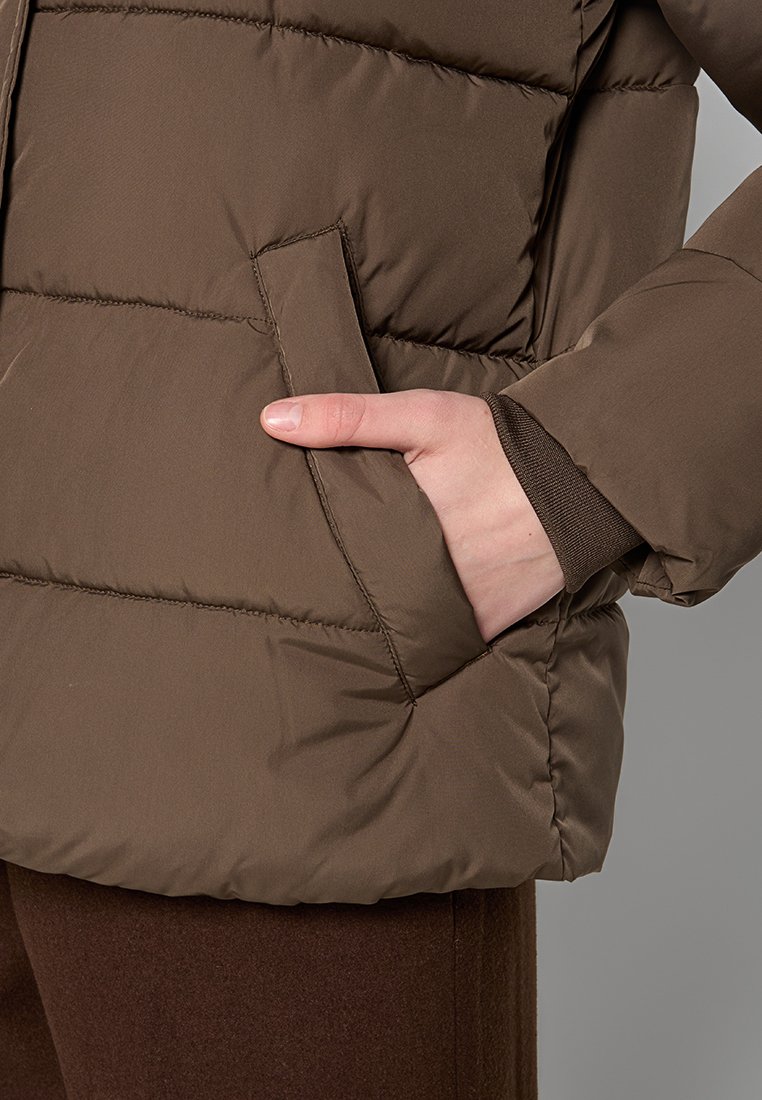 Giubbotto puffer marrone con design cucito e tasca laterale. Tessuto liscio e resistente con una texture leggermente lucida. Presenta una vestibilità rilassata.