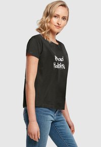 Sort bomulds T-shirt med korte �ærmer; prydet med teksten "Bad Habits" i hvid, flosset skrifttype på forsiden. Klassisk rund halsudskæring.