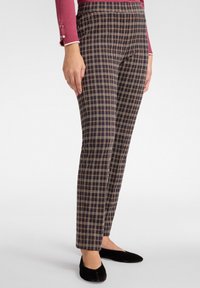 Spodnie w kratę w kolorze granatowym z złotymi i brązowymi liniami, slim fit, o gładkiej powierzchni i bocznymi kieszeniami. Noszone z czarnymi płaskimi butami.