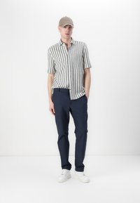 Camicia a maniche corte a righe in bianco e blu navy, abbinata a pantaloni blu navy e sneakers bianche. Presenta un colletto con bottoni e una vestibilità morbida.