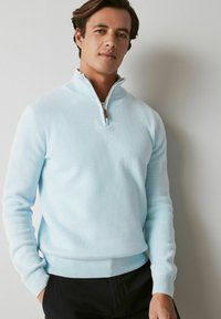 Šviesiai mėlynas ketvirčio užtrauktuko megztinis, pagamintas iš tekstūruotos medžiagos, su taškytais rankogaliais ir apdaila, taip pat odiniu užtrauktuko traukikliu.