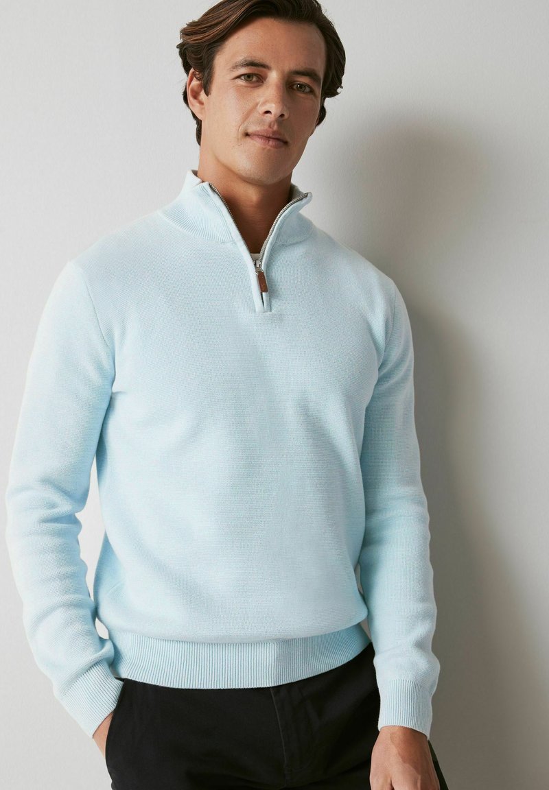 Šviesiai mėlynas ketvirčio užtrauktuko megztinis, pagamintas iš tekstūruotos medžiagos, su taškytais rankogaliais ir apdaila, taip pat odiniu užtrauktuko traukikliu.