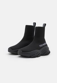 Stivaletti alla caviglia neri in maglia con bordo a coste, suola nera spessa e logo "STEVE MADDEN" bianco sul lato. Design testurizzato e calzata aderente.