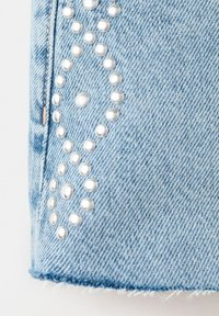 Tissu denim bleu clair avec des clous ronds argentés disposés en deux formes losanges près de la couture et du bord effiloché.