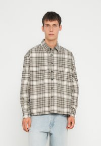 Ruudullinen paita beige, musta ja valkoinen sävy. Napitettava malli, jossa on rintatasku ja pitkät hihat. Valmistettu teksturoitua kangasta.