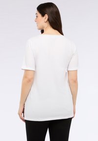 Camiseta blanca de manga corta con un corte relajado, que presenta mangas enrolladas y un dobladillo curvado, confeccionada en un tejido suave y liso.