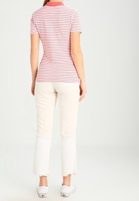 Poloko s krátkým rukávem, červené a bílé pruhované, s límečkem, v kombinaci s krémovými rozšířenými kalhotami s bílým lemem a třepeným okrajem. Bílé tenisky.