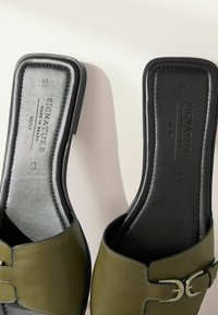 Sandales à glissière en cuir vert avec une large bride et un détail de boucle argentée, dotées d'une semelle intérieure noire texturée et d'une semelle lisse.