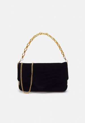 Pochette en velours noir avec motif matelassé en chevrons, anse chaîne épaisse en or et une bandoulière supplémentaire fine chaîne en or sur fond uni.