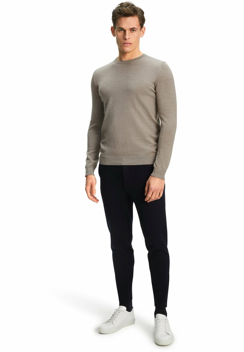 Hellgrauer Strickpullover mit langen Ärmeln und rundem Ausschnitt, kombiniert mit dunklen Hosen und weißen Sneakers. Glatte Textur, taillierte Passform.