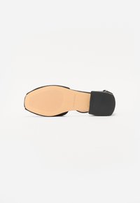 Musthave musta sandaal tekstureeritud pealse ja sileda talla ning plokk kontsaga. Omab reguleeritavat rihma, rõhutades minimalismi disaini.