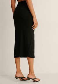 Musta ribbed midi-hame, jossa on istuva siluetti, sileä tekstuuri ja korkea vyötärö. Yhdistetty mustiin nilkkureihin, joissa on korot ja strapsit.