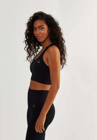Soutien-gorge de sport noir avec une texture côtelée et un logo en forme de cœur, associé à des leggings taille haute assortis ; design épuré, style minimaliste.