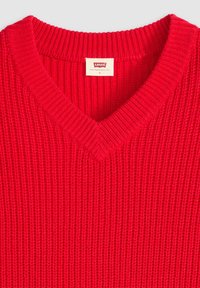 Czerwony sweter z dzianiny z dekoltem w serek, charakteryzujący się prążkowaną fakturą i metką z napisem "Levi's" na wewnętrznym kołnierzu. Rozmiar oznaczony jako mały.