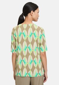 Short-sleeve top in soft, lightweight fabric featuring a geometric pattern in green, turquoise, beige, and white, with a relaxed fit.