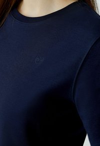 Navyblauwe aansluitende sweatshirt met een ronde hals, gemaakt van een gladde stof. Heeft een klein hartlogo geborduurd op de borst.