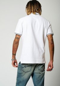 Polo shirt blanc à manches courtes avec un motif texturé et une finition à rayures contrastantes au col et aux poignets, associé à un jean en denim bleu.