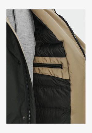 Zielona i beżowa kurtka wewnątrz ma pikowaną czarną podszewkę, szary materiał z tyłu oraz jedną kieszeń na zamek błyskawiczny w beżowej części.