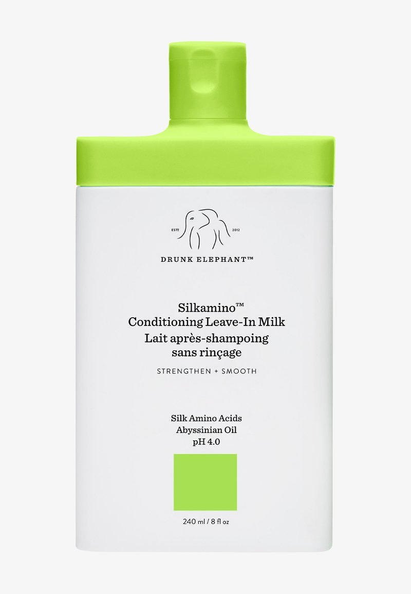 Weiße Flasche mit einem leuchtend grünen Deckel, beschriftet mit "Silkamino™ Conditioning Leave-In Milk", die Produktdetails und das Logo von Drunk Elephant zeigt.