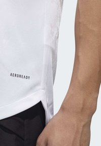 Hvid AEROREADY atletisk skjorte i tekstureret stof, med sideslids i kanten, der viser et nærbillede af ærmet og armen.