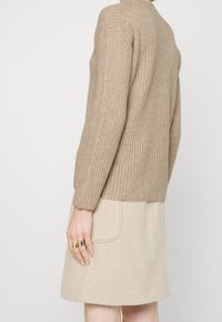 Pull beige en tricot à manches longues, texture côtelée et encolure ronde, assorti à une jupe en laine beige avec une poche latérale.