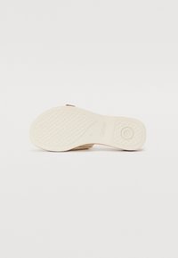 Semelle d'une sandale beige montrant une prise texturée, un motif circulaire près du talon, et le nom de la marque "Gabor" sur une semelle lisse de couleur claire.