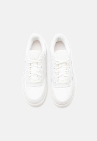 Ζευγάρι καθαρών λευκών αθλητικών παπουτσιών με κορδόνια, εμφάνιση από πάνω σε ένα απλό ανοιχτό γκρι φόντο.