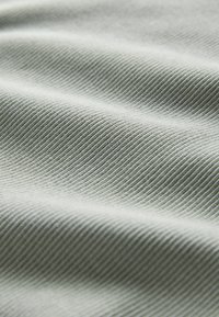 Detail svetlosivého rebrovaného látky s jemnými záhybmi a viditeľnými diagonálnymi textúrnymi líniami.