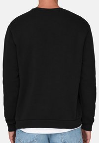 Sweatshirt noir à col rond, avec des poignets et une ceinture côtelés. L'arrière présente une texture lisse, et il est associé à un jean bleu clair.