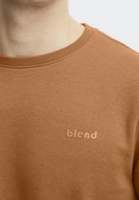 Hnědá mikina s kulatým výstřihem, s hladkou texturou a jemným logem "blend" v odpovídající barvě na levé straně.