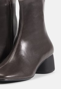 Dark brown leather ankle boots with a smooth texture, a side zipper, and a rounded heel. Sleek design with a modern silhouette.