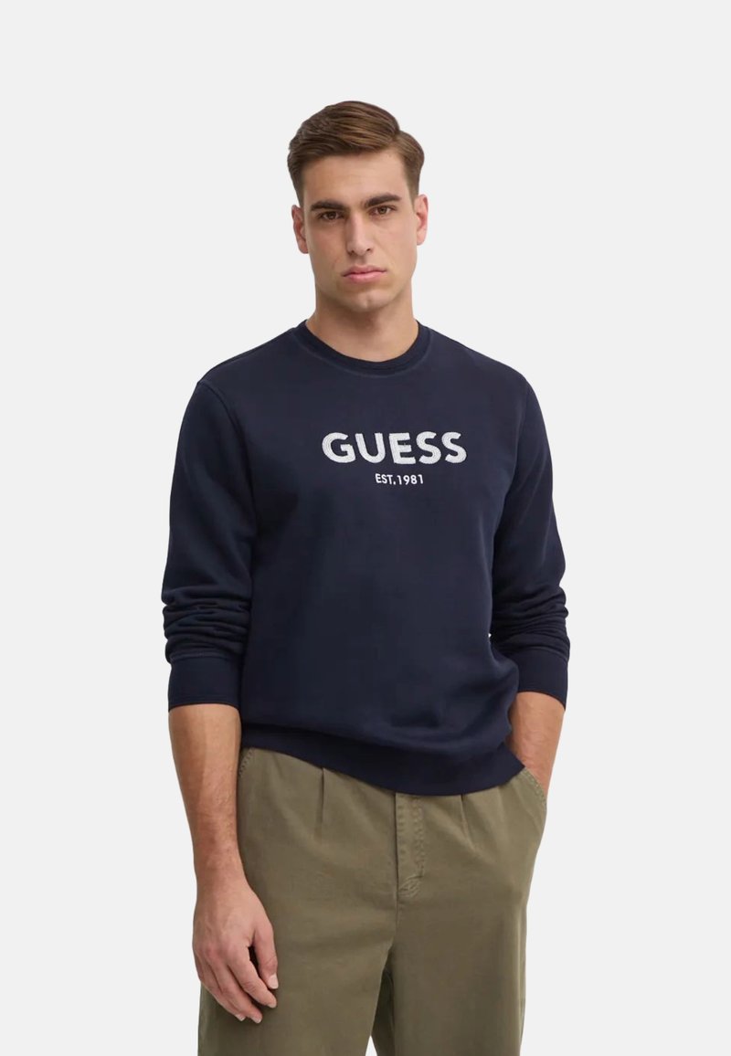 Felpa blu navy con collo tondo e polsini a coste, con il logo "GUESS EST. 1981" stampato in bianco sul petto. Tessuto in cotone misto tessurato.