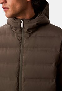 Chaqueta acolchada de color verde oliva con cuello alto, cierre frontal de cremallera y sutil branding de Calvin Klein en impresión tonal en toda la tela.
