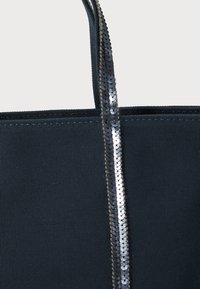 Bolsa de lona negra con detalles de lentejuelas plateadas brillantes en la correa. Tela resistente y diseño estructurado sin adornos visibles.