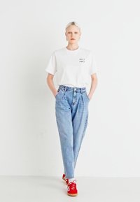 Hvit t-skjorte med kort arm som har teksten "KEEP IT SIMPLE", lyseblå høy midje jeans og røde joggesko med hvite detaljer.