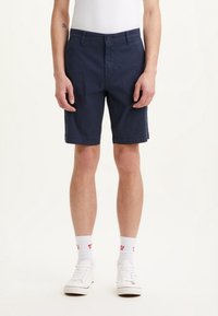 Mörkblå bomullsshorts med rak skärning, knappstängning och sidofickor, i kombination med vita strumpor och sneakers.