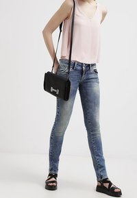 Woman wearing light pink sleeveless top, faded blue skinny jeans, black crossbody bag, and black platform sandals.