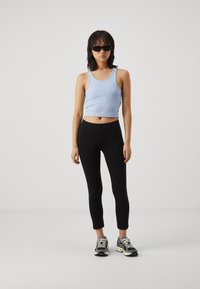 Světle modrý uplý crop top s jemným žebrováním v kombinaci s černými legínami a šedými teniskami s bílými tkaničkami. Modelka nosí černé sluneční brýle.
