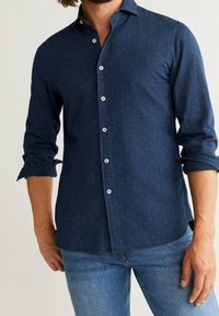 Camicia blu navy con bottoni, caratterizzata da un motivo sottile, maniche lunghe arrotolate, realizzata in stoffa tessuta; presenta bottoni bianchi e un colletto strutturato.