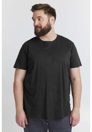 Camiseta negra de manga corta fabricada en un tejido suave, con cuello redondo y un corte holgado, combinada con pantalones oscuros texturizados.