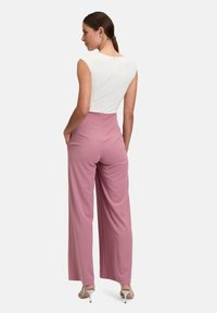 Biały top z krótkim rękawem w kształcie litery cap połączony z różowymi spodniami o wysokim stanie i szerokich nogawkach. Gładki materiał i subtelny zamek błyskawiczny z tyłu. Srebrne szpilki.