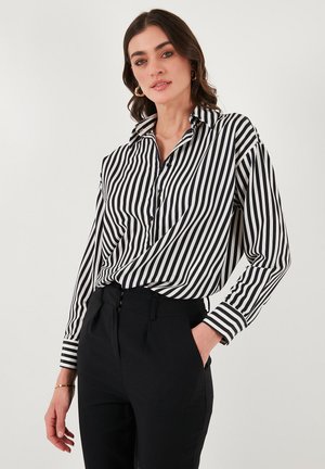 Black and white striped button-up shirt with long sleeves and a collar, featuring a relaxed fit and contrasting cuffs, paired with black trousers.