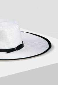 Szerokoskrzydły kapelusz z białego plecionego słomy, z czarną wstążką i akcentującą klamrą, o gładkiej fakturze i okrągłym kształcie.