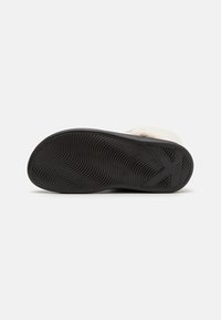 Suela de goma negra con un patrón de olas texturizado; suave forro de piel sintética color crema visible a lo largo del borde superior.