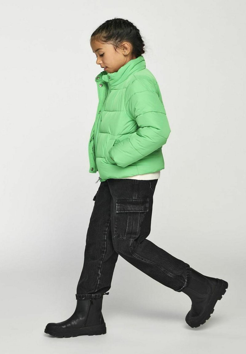 Green puffer jacket with a high collar, zip closure, and two side pockets, paired with black cargo pants and black ankle boots.