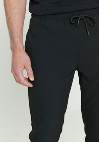 Zwarte joggerbroeken met een elastische tailleband en een trekkoord. De stof is glad, en het ontwerp heeft zijzakken.