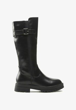 Schwarzer kniehoher Lederstiefel mit grober Sohle und dekorativem Schnallenriemen oben, Seitenansicht vor weißem Hintergrund.