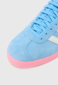 Baskets en daim bleu avec semelle en caoutchouc rose, dotées de lacets plats, de rayures sur les côtés et d'un design de bout arrondi.
