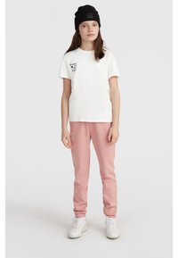 Vit bomullströja med svart text och design, ihop med rosa sweatpants med vit text. Svart stickad mössa och vita sneakers.